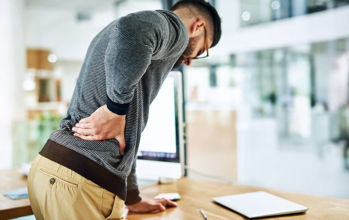 Office worker holding his lower back due to discomfort after standing at his desk.